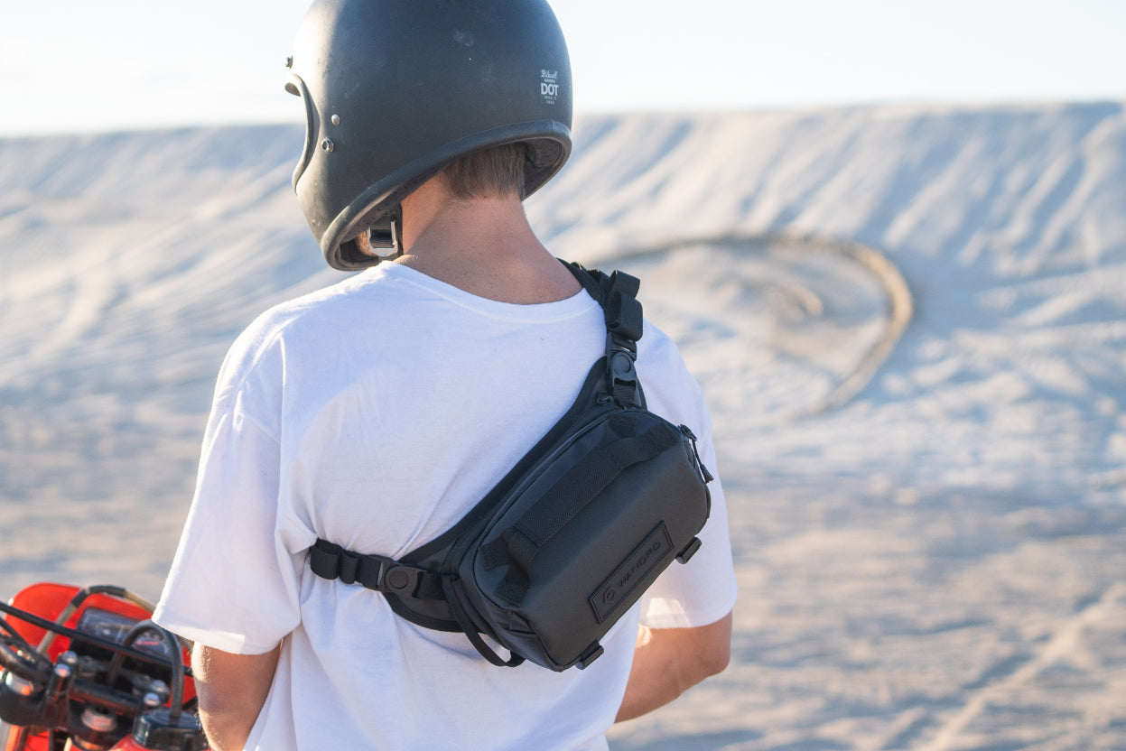 Person wearing a helmet and carrying a black bag in a desert setting