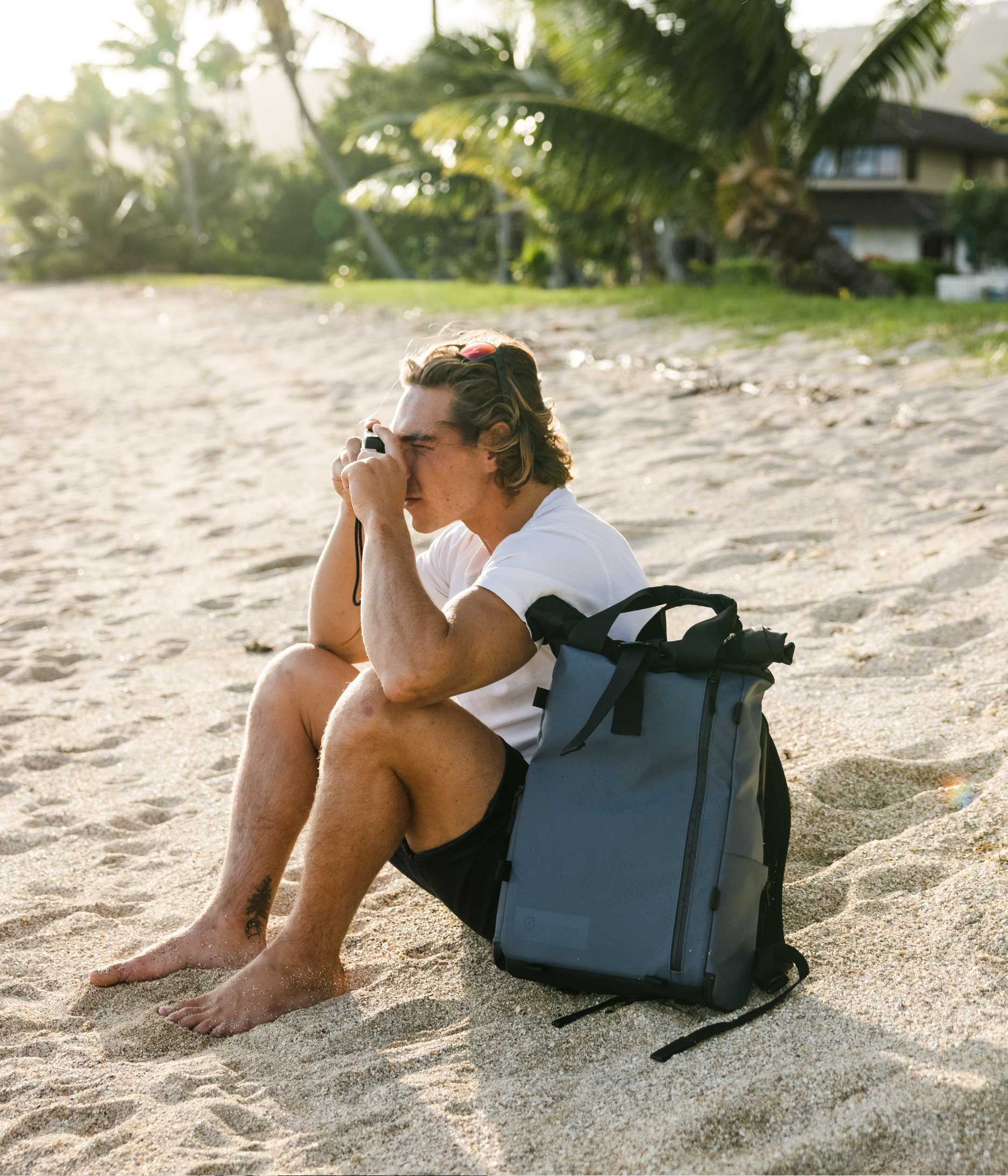 Man sitting by the beach with his backpack while taking a Photo